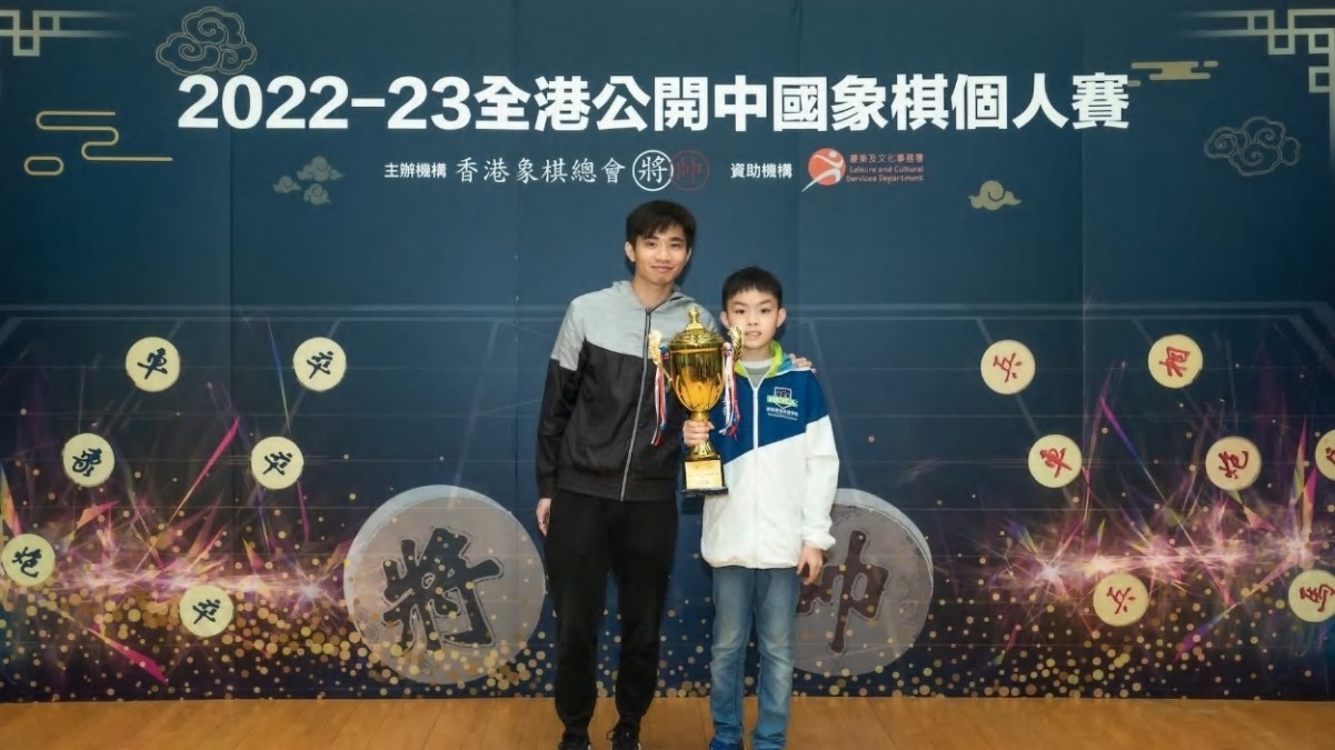年僅 11 歲的蔡時泓（右）力壓眾多選手獲得丙組冠軍，香港象棋特級大師黃學謙為其頒發獎項。